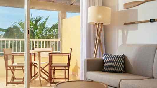 En indretning med sofa og pude i forgrunden samt udsigt til en møbleret altan. (AI-genereret tekst)