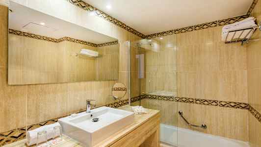 Et moderne badeværelse med fliser, en rektangulær vask, et stort spejl og et badekar med glasvæg. (AI-genereret tekst)