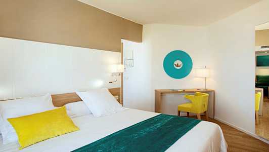 Et moderne hotelværelse med en seng i forgrunden, en skrivebordshjørne med en gul stol og en blå dekorativ vægdetalje. (AI-genereret tekst)