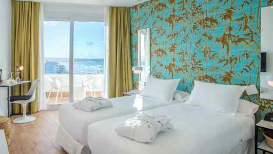 Et hotelværelse med to hvide senge og balkon med udsigt mod havet. (AI-genereret tekst)