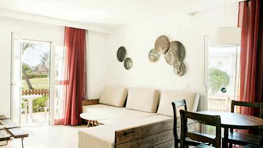 En stue med lyse møbler, et stort vindue med røde gardiner og dekorationer på væggen. (AI-genereret tekst)