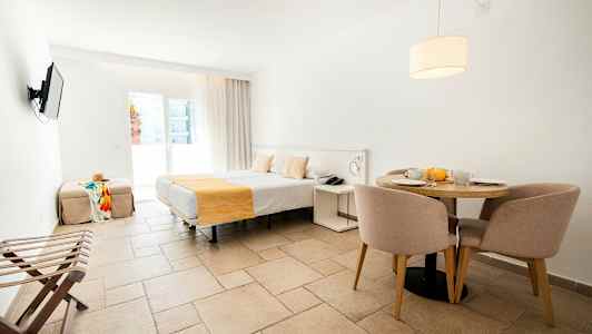 Et hotelværelse med en seng, et spisebord med stole og en tv på væggen. (AI-genereret tekst)