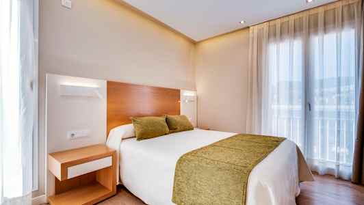 Et hotelværelse med en dobbeltseng med grønne puder og sengetæppe. Et natbord står ved siden af sengen. (AI-genereret tekst)