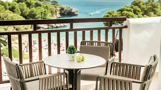 Altan med bord og stole vendt mod havet, stranden og frodige træer. (AI-genereret tekst)