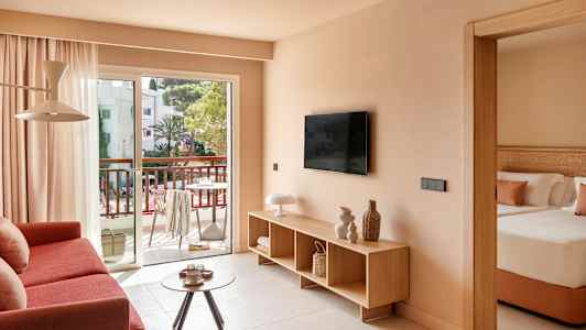 Stue med sofa, TV og udgang til altan, samt et delvist synligt soveværelse. (AI-genereret tekst)