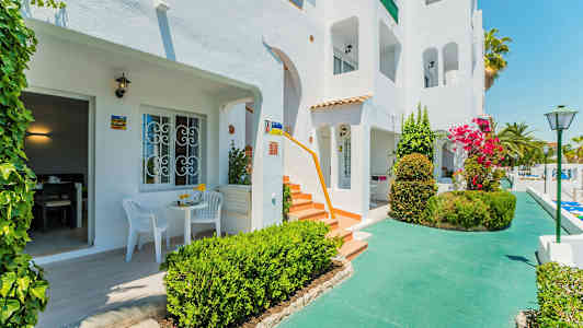 Hvid bygning med terrasser og frodige omgivelser. (AI-genereret tekst)