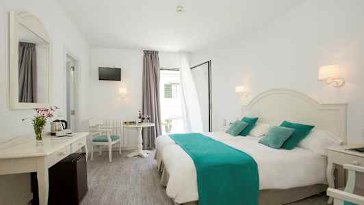 Et lyst hotelværelse med dobbeltseng med hvide lagner og turkise detaljer, bord med stole samt et spejl og TV. (AI-genereret tekst)