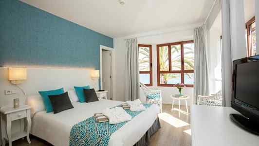 Hotelværelse med dobbeltseng, vinduer og udsigt over havet. (AI-genereret tekst)