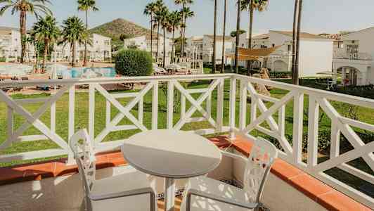 Udsigt fra en altan med hvide havemøbler, mod en have med pool og palmer. (AI-genereret tekst)