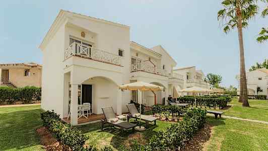 Hotellets hvide to-etages bygninger med altaner og gårdhaver omgivet af grønne områder. (AI-genereret tekst)