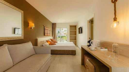 Et hotelværelse med en sofa, en seng, et skrivebord med kaffemaskine og glas samt en dør til en altan. (AI-genereret tekst)