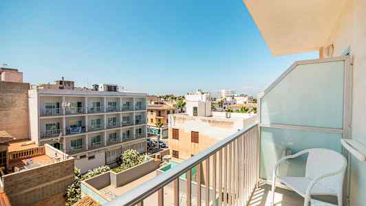 Udsigt fra en altan med boligbygninger og træer under en klar blå himmel. (AI-genereret tekst)