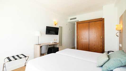 Hotelværelse med to enkeltsenge, skrivebord, stol, TV og garderobe. (AI-genereret tekst)