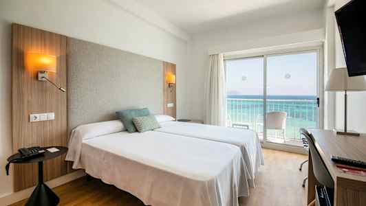 Hotelværelse med to senge, havudsigt gennem en glasdør og skrivebord. (AI-genereret tekst)