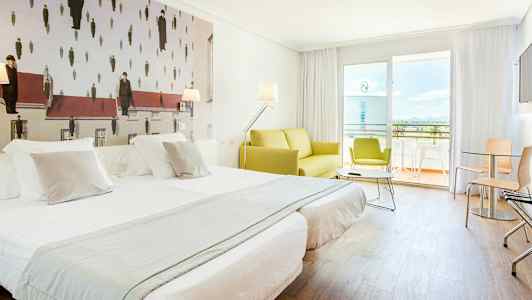 Et hotelværelse med to opdækkede enkeltsenge, en grøn sofa og en balkon i baggrunden. Væggudsmykningen har et kunstværk med et usædvanligt design. (AI-genereret tekst)