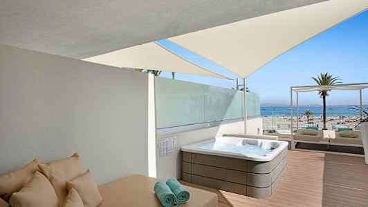 En solterrasse med en jacuzzi, solseng og udsigt til stranden og havet. (AI-genereret tekst)