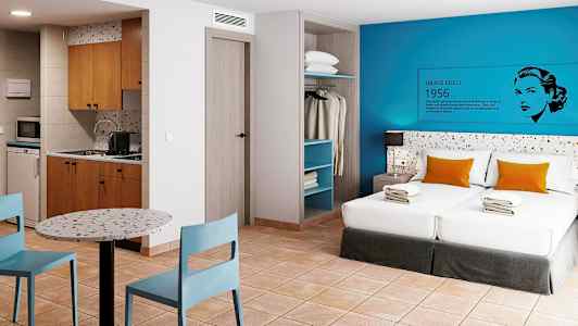 Et hotelværelse med to senge, køkken, spisebord og åben garderobe. (AI-genereret tekst)