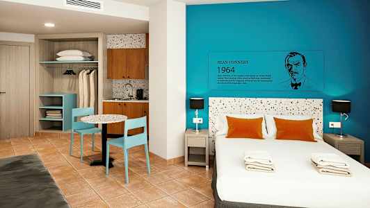 Et moderne hotelværelse med en dobbeltseng, blå vægge og en lille køkkenkrog. (AI-genereret tekst)