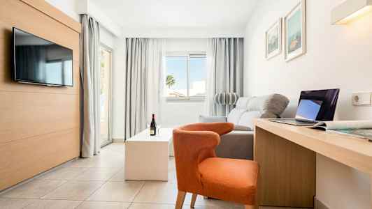 Lyst, moderne hotelværelse med sofa, stol, TV, skrivebord og store vinduer. (AI-genereret tekst)