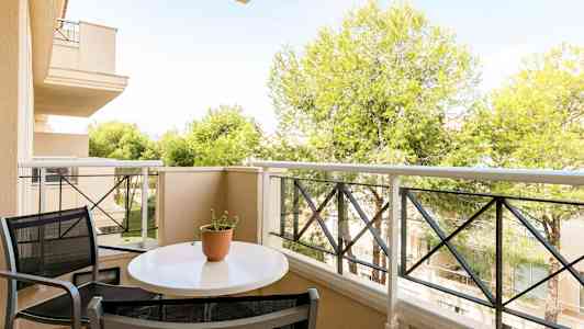 En altan med et bord og stole samt udsigt til træer og bygninger. (AI-genereret tekst)