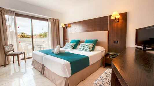 Et hotelværelse med to enkeltsenge, et tv og en altan i baggrunden. (AI-genereret tekst)