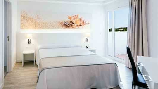 Et hotelværelse med dobbeltseng, hvid og beige indretning, dekoration med muslingeskaller over sengen. (AI-genereret tekst)