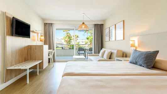 Et hotelværelse med to senge, en siddegruppe og balkon med udsigt. (AI-genereret tekst)