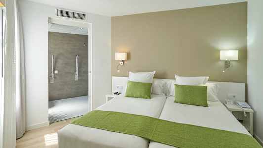 Hotelværelse med to enkeltsenge, grønt sengetøj og åbning til badeværelset. (AI-genereret tekst)