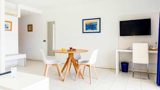 Et lyst rum med et rundt spisebord og stole, et TV på væggen og en arbejdsplads med en stol. (AI-genereret tekst)