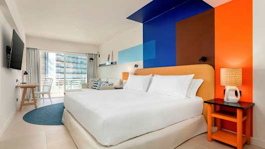 Et hotelværelse med en dobbeltseng, farverigt vægdesign og en altan. (AI-genereret tekst)