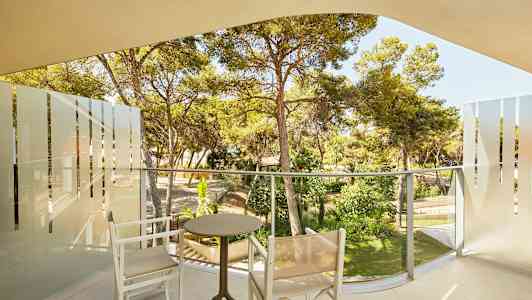 En altan med to stole og et bord, med udsigt til en frodig have. (AI-genereret tekst)