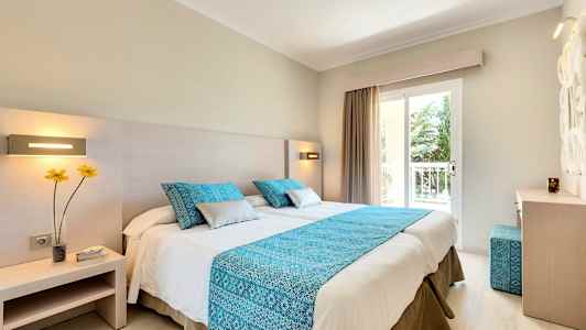 Et hotelværelse med en dobbeltseng, blå dekorative puder og et blåt sengetæppe. (AI-genereret tekst)