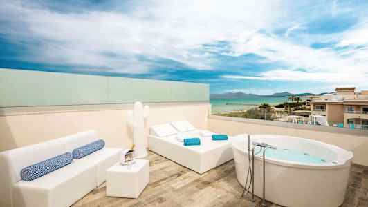 Tagterrasse med havudsigt, udstyret med jacuzzi, liggestole og sofamiljø. (AI-genereret tekst)
