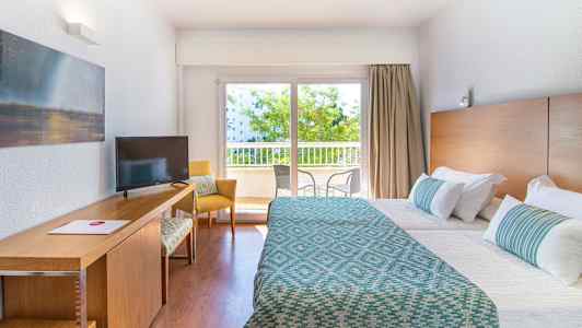 Hotelværelse med to senge, skrivebord og vindue med udsigt til altan. (AI-genereret tekst)
