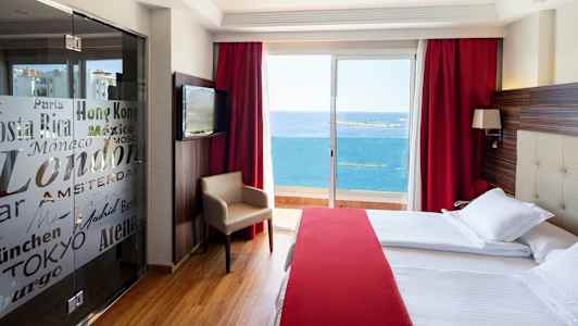 Et hotelværelse med store senge, rødt interiør og en altan med udsigt over havet. (AI-genereret tekst)