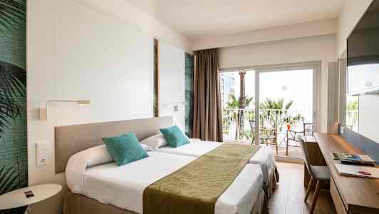 Hotelværelse med to enkeltsenge, skrivebord og altan med udsigt til palmer. (AI-genereret tekst)