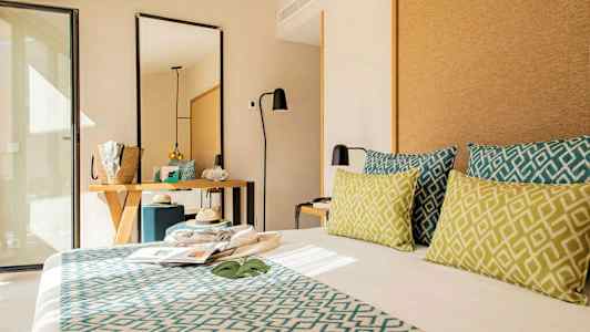 Hotelværelse med moderne indretning, seng med dekorative puder, spejl og skrivebord. (AI-genereret tekst)