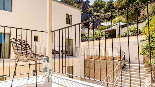 En altan med en stol og et gelænder, omgivet af en bygning og beplantning. (AI-genereret tekst)