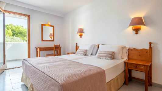 Et hotelværelse med en dobbeltseng, to sengelamper, et skrivebord, en stol og en balkon. (AI-genereret tekst)