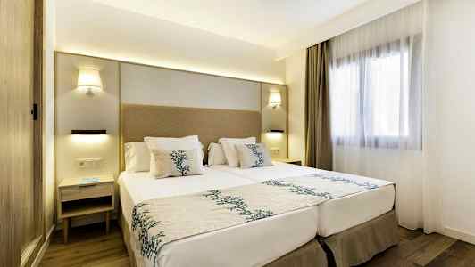 Moderne indrettet hotelværelse med en dobbeltseng, natbord og et vindue med lyse gardiner. (AI-genereret tekst)