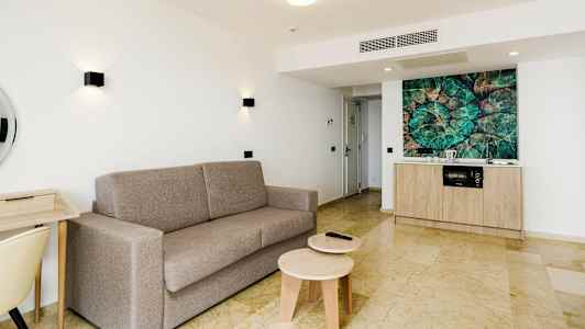 Lys lejlighed med grå sofa, skrivebord og køkkenområde. (AI-genereret tekst)