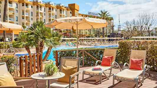 Udendørsområde ved pool med liggestole og parasoller, hotelbygning i baggrunden. (AI-genereret tekst)