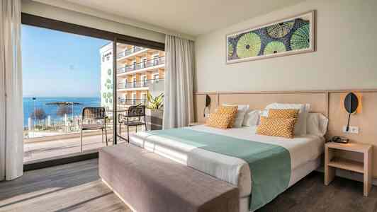 Hotelværelse med seng, siddepladser og udsigt til havet gennem store vinduer. (AI-genereret tekst)