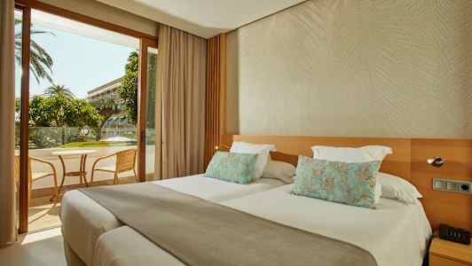 Hotelværelse med to separate senge og udsigt til en møbleret balkon. (AI-genereret tekst)