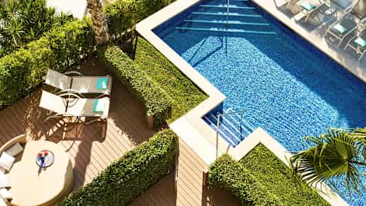 Et poolområde med liggestole og grønne buske. (AI-genereret tekst)