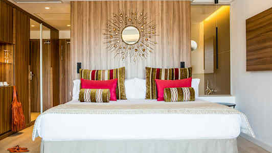 Moderne hotelværelse med en stor seng, dekorative puder i forskellige farver og træpanel på væggen bagved. (AI-genereret tekst)