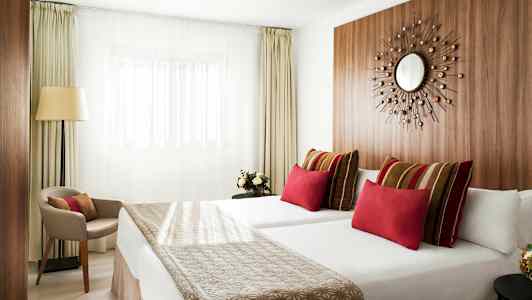 Moderne hotelværelse med to senge, farverige puder og minimalistisk indretning. (AI-genereret tekst)