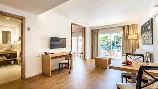 En moderne hotel-suite med siddegruppe, spisebord, TV og åbning til altan med udsigt. (AI-genereret tekst)