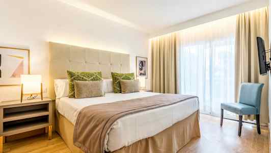 Et hotelværelse med en dobbeltseng, sidebord, stol og stort vindue. (AI-genereret tekst)