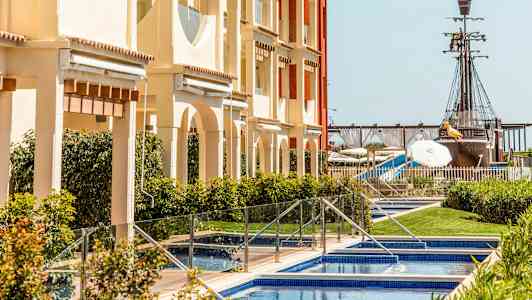 En bygning med swimmingpools foran, og i baggrunden ses et piratskib. (AI-genereret tekst)